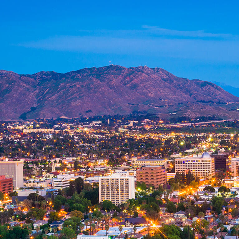 Evening aerial view of Riverside, California, with city lights and surrounding mountains.