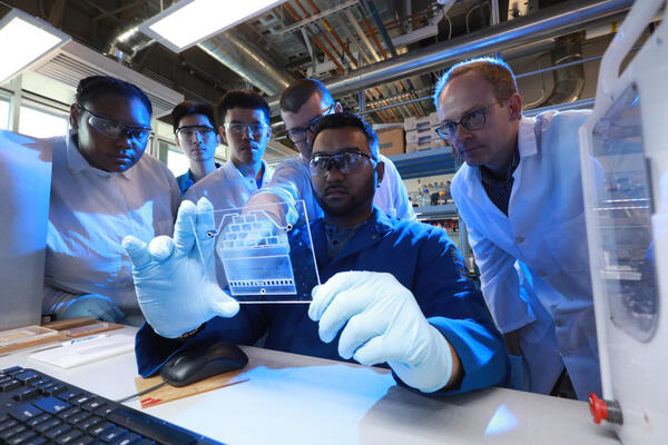 Engineering students and a faculty researcher collaborate in a laboratory, examining data and equipment during a hands-on research project.